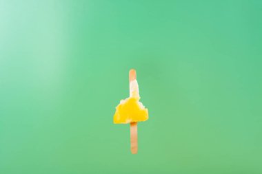 yellow popsicle with mostly eaten on a light green background clipart