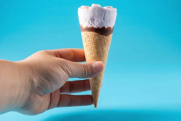 手拿着一个花生冰淇淋锥在蓝色背景 — 图库照片