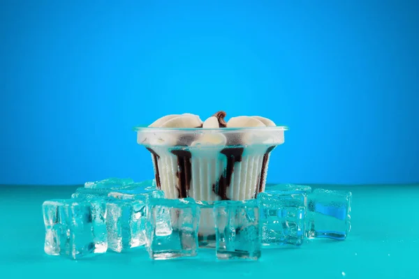 backlit cup of ice cream and ice cubes on blue background