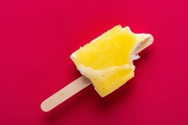 yellow popsicle with a couple of bites on a red background clipart