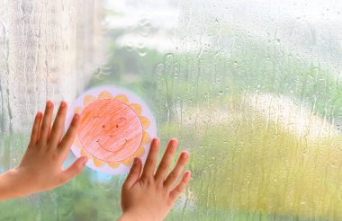 inanç ve iyimserlik yağmur bir gün kavramı içinde gülümseyen bir güneş resmi tutan çocuk