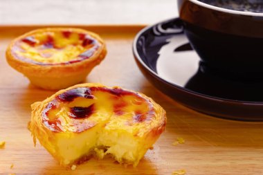 Çeyrek kesilmiş taze Portekiz yumurtalı tartlar ve arkasında bir fincan kahve.