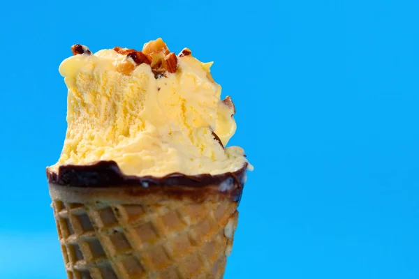 close up of mango and chocolate flavor ice cream cone with peanut with couple of bites on blue background