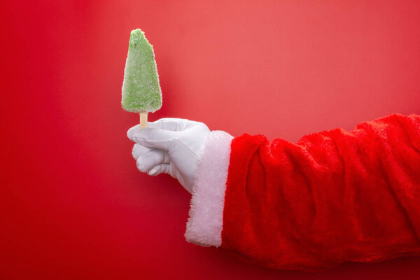 santa claus holding a green bean popsicle with a bite in front of a red background