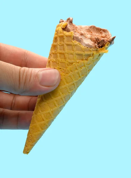 手拿着巧克力味冰淇淋蛋筒 蓝底上有一些咬痕 — 图库照片