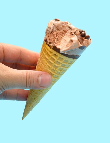 手拿着新鲜的巧克力味冰淇淋蛋筒 在蓝色的背景上咬了一口 — 图库照片