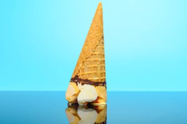 Taze vanilya ve çilek aromalı dondurma külahı yansımalı bir bardağın üstünde baş aşağı duruyor.