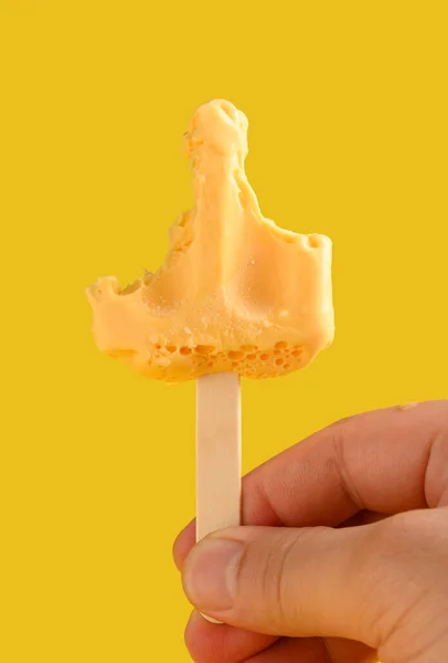 手拿着芒果布丁味冰棒 最后一点在黄色背景上 — 图库照片
