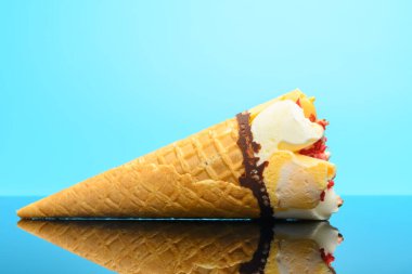 Yandan bakıldığında taze vanilyalı ve çilekli dondurma külahı yansımalı bir bardakta.