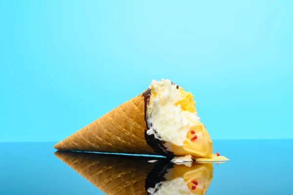 vanilla and strawberry flavor ice cream cone with couple of bites on a glass with reflection