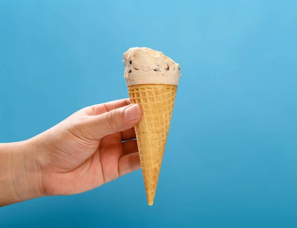 手拿着奶茶味冰淇淋筒 上面有一些蓝色背景的水平成分 — 图库照片