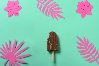 En üstteki çikolatalı buzlu şeker. Üzerinde kağıt, çiçek ve yeşil arka planda yapraklar var.