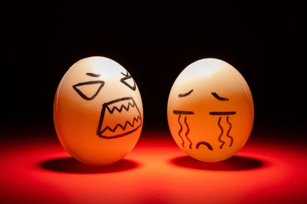egg faces of an angry one blaming a crying one highlighted in dark