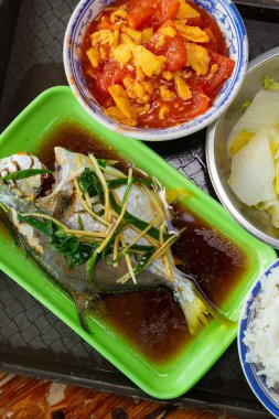 Üst görünüm gümüş pomfret, karışık pirinç, karıştırılmış domates ve çırpılmış yumurta içeren dengeli bir Asya yemeği, dikey kompozisyonda bir tepside servis edilir.