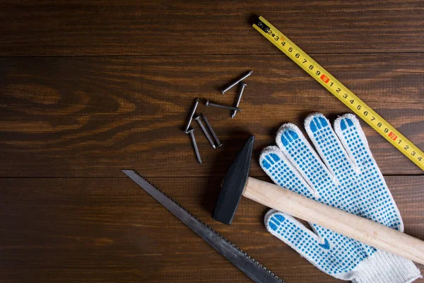 Gebouw tools. Hamer, spijkers, ijzerzaag, rolmaat en handschoenen op een houten achtergrond — Stockfoto