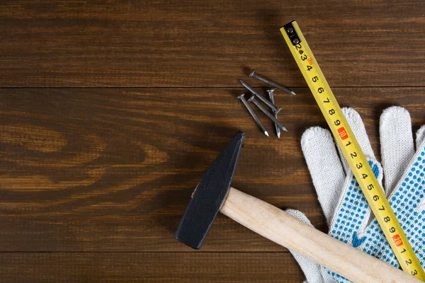 Gebouw tools. Hamer, spijkers, meetlint en handschoenen op een houten achtergrond — Stockfoto
