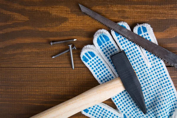 Building tools. Hammer, nails, hacksaw and gloves on a wooden background