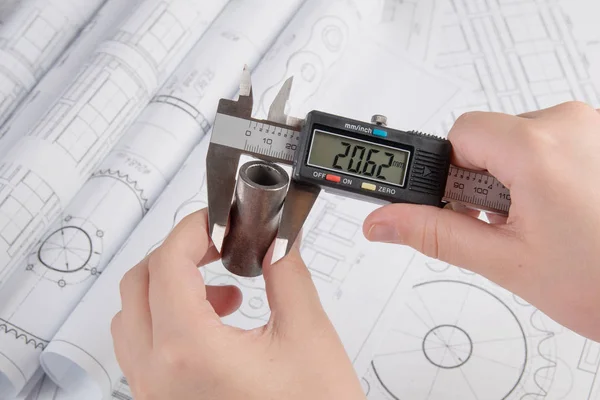 Trabalho de engenheiro. Medição da peça metálica com uma pinça no fundo de desenhos de engenharia — Fotografia de Stock