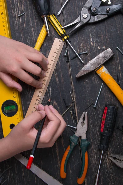 Matita in mano a un ingegnere e costruttore. Vecchi strumenti di costruzione casa su un tavolo di legno scuro . — Foto Stock