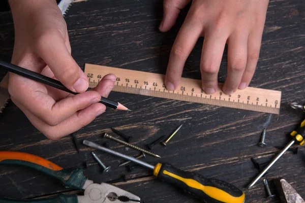 Matita in mano a un ingegnere e costruttore. Vecchi strumenti di costruzione casa su un tavolo di legno scuro . — Foto Stock