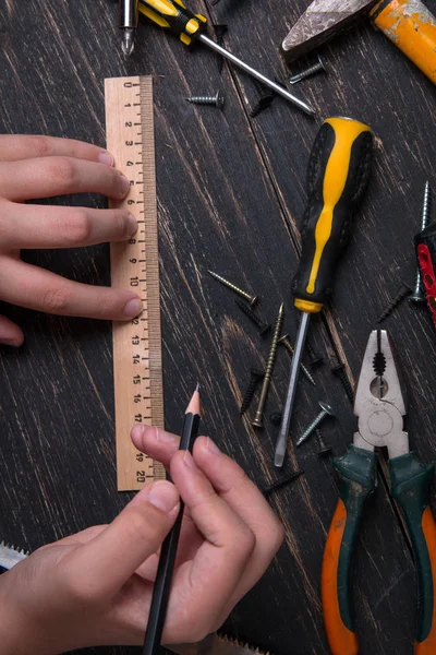 Ołówek w ręku inżyniera i budowniczego. Stare narzędzia do budowy domu na ciemnym drewnianym stole. — Zdjęcie stockowe