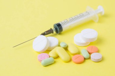 sarı bir arka plan üzerinde ilaç hapları, ilaçlar, şırınga ve antibiyotikler