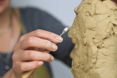 Heykeltraş sanatçı bir büstü heykel kil ile oluşturma. O işlerinin çok mutlu, konsantre, o bir kadın heykel. heykel ön plan var. İş yerinde heykeltıraş.
