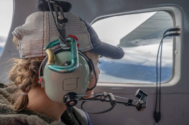 Female passenger looks out the window while flying in an Alaskan Bush Plane, wearing a headset clipart