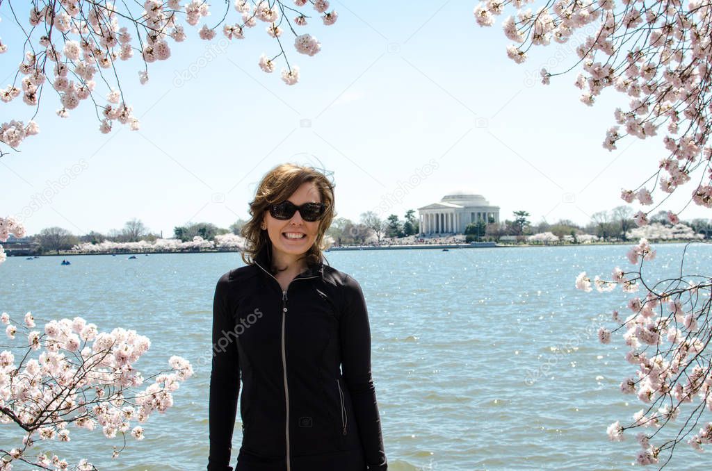 Adult woman stands and poses by Cherry Blossom trees and the Thomas Jefferson Memorial, natural frame with the trees