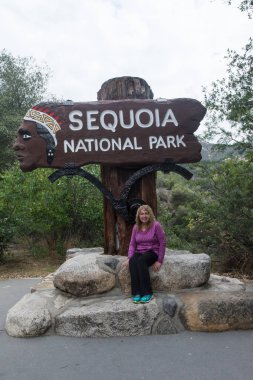 22 Mayıs 2018 - Sequoia, California: California Sequoia National Park için oturum açın. Kadın kıdemli Orta (60'ların) yaşlı turist yetişkin kadın işareti ile poz veriyor