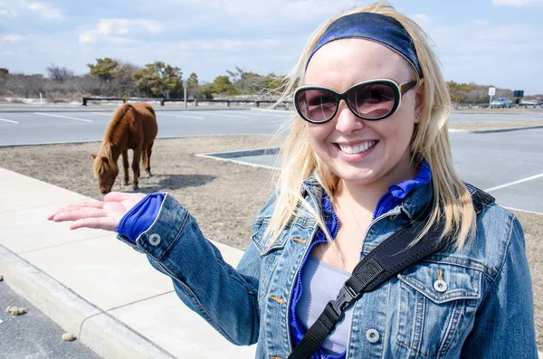 Forced perspective of a blonde woman making a wild horse in a parking lot appear to eat out of her hand.