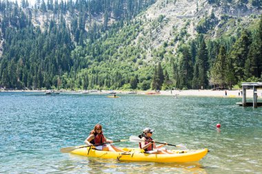 Two female friends row in a dual kayak on Lake Tahoe in Emerald Bay. Concept for teamwork, female friendship, working together clipart