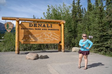 1 Ağustos 2018 - Denali Milli Parkı Alaska: bir selfie sopa ile onu smartphone park giriş işareti bir fotoğraf çekmek için bir sarışın turist kadın kullanır