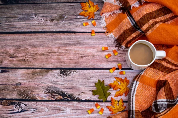 Cozy autumn coffee flat lay background with orange plaid blanket, candy corn, coffee cup and leaves. Wooden backdrop