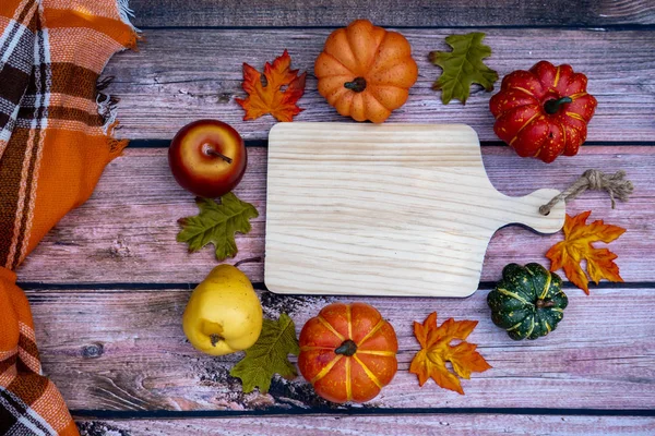 Cozy fall autumn concept featuring wooden cutting board for copy space, surrounded by pumpkins and gourds. Plaid blanket and wood background