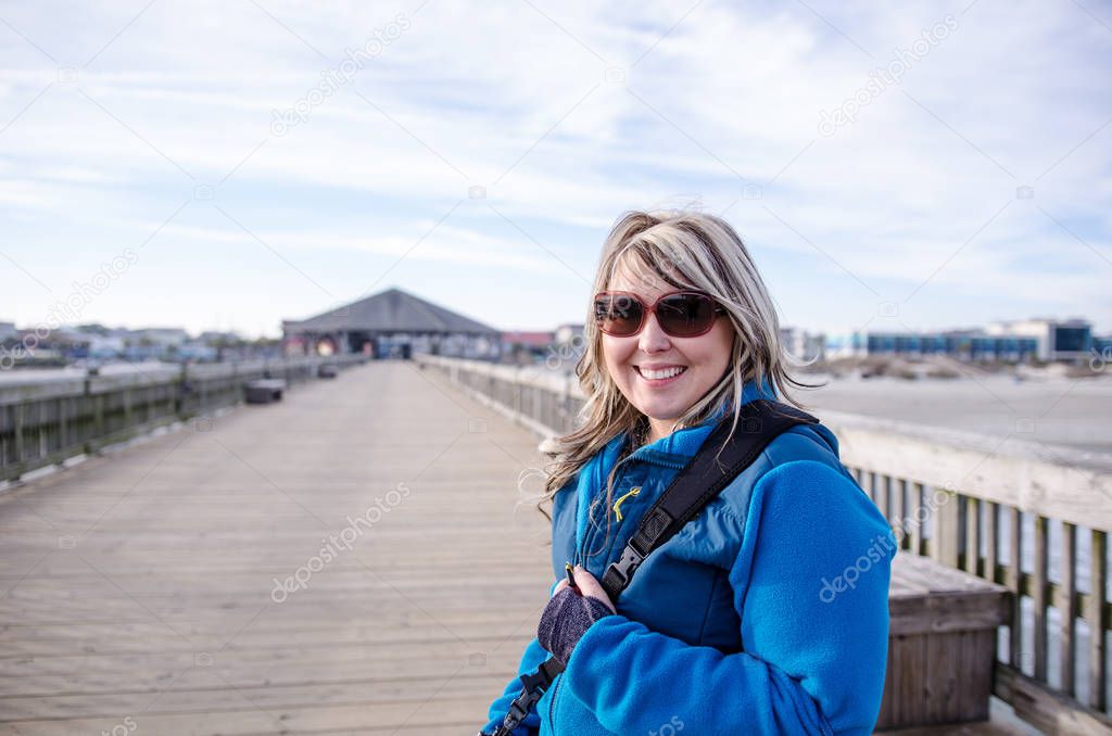 Pretty blond adult female stands on the Tybee Island pier, bundled up in a winter jacket