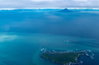 Teal waters of Alaska near Katmai National Park, with view of Augustine Island and the Aleutian Range of mountains. Aerial photography view clipart