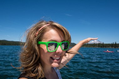 Forced perspective of a female holding her hand appears to be touching Mt. Bachelor in the distance from Lava Lake along the Cascade Lakes Scenic Byway. Girl is smiling clipart