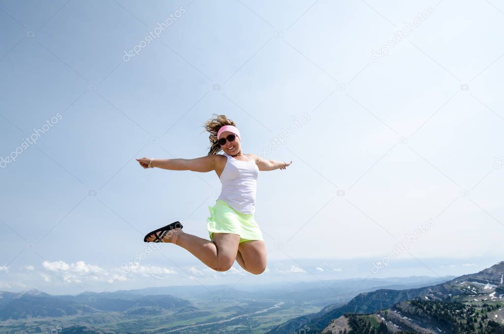 Happy excited young woman jumps on top of the Grand Teton Mountains in Jackson Hole Wyoming in the summer. Concept for freedom, travel
