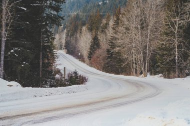 Icy, snow covered road along the Bow Valley Parkway in Winter in Banff National Park Canada clipart