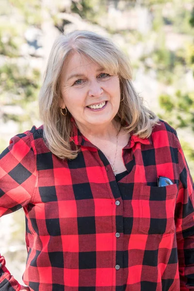 A mature blonde woman wearing a buffalo plaid flannel shirt (red and black) poses for a portrait in the Eastern Sierra Nevada mountains in California, on top of Devil\'s Postpile National Monument