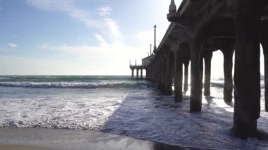 Güney Kaliforniya'daki Manhattan Beach İskelesi'nde öğleden sonra güneşi dalgalar kumsala çarpar. 4k video