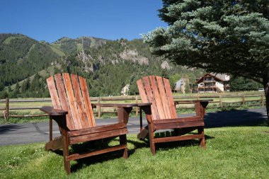 Two empty wood adirondack chairs sit on grass, overlooking the S clipart