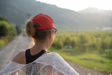 Woman wearing a red ballcap and a white lace shawl looks out on  clipart