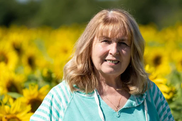 Senior woman (60-65 years) poses in front of a field of sunflowe