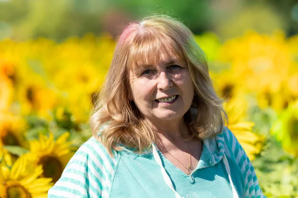 Senior woman (60-65 years) poses in front of a field of sunflowe