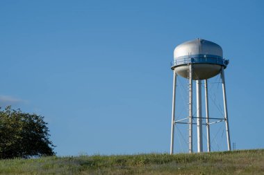 Watertower in a field against a blue sky.  clipart