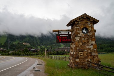 Teton Village, Wyoming - June 25, 2020: Sign welcoming visitors and tourists to the popular ski village town in the Grand Tetons mountain range. Road leading into town clipart