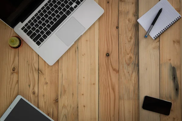 Wood office desk table with laptop, paper,  smartphone, tablet and pen. Top view with copy space.