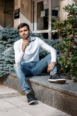 Genç bir adam şehrin sokaklarında dolaşıyor. Çocuk güneş gözlüğü şık adamın binanın yanında. Adam bir kamçı üzerinde oturur. Sakal ve saç, şık bir adamda.